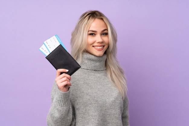 Teenager girl over purple wall happy in vacation with passport and plane tickets