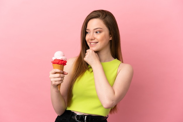 Teenager girl with a cornet ice cream over isolated pink background looking to the side and smiling