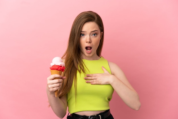 Teenager girl with a cornet ice cream over isolated pink background surprised and shocked while looking right