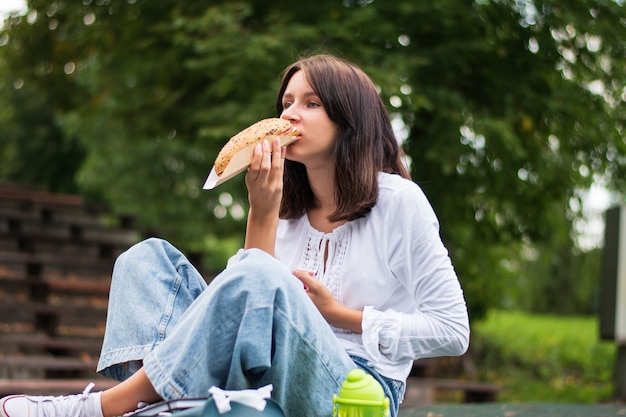 A teenager is eating a sandwich in the park