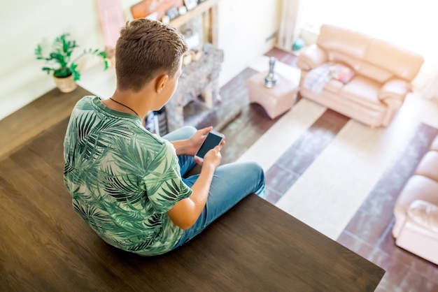 The teenager is using cell phone sitting on the second floor of the house top