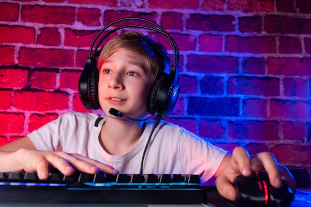 A teenager at a keyboard with headphones playing video games at a desk