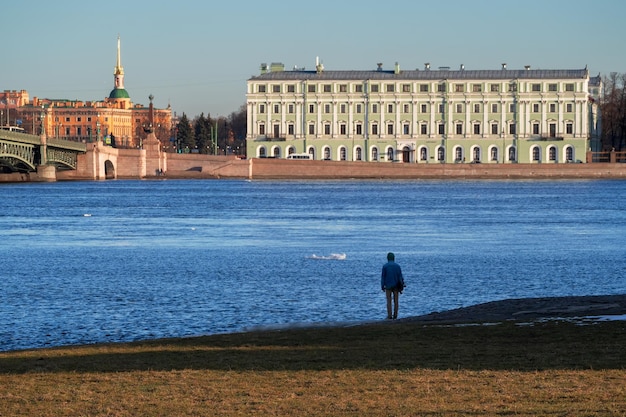 Teenager looks over the blue river of Neva in St Petersburg Russia Back view Architecture of embankments of rivers and canals of St Petersburg