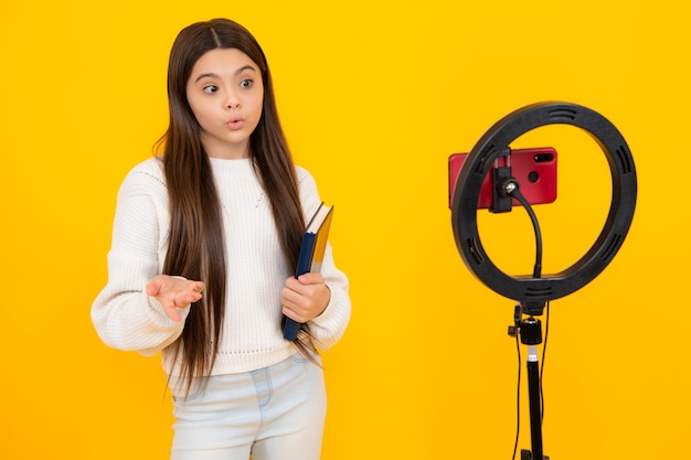 Teenager recording online media video Teen girl streaming online and sharing social media content by mobile phone app network isolated on yellow studio background