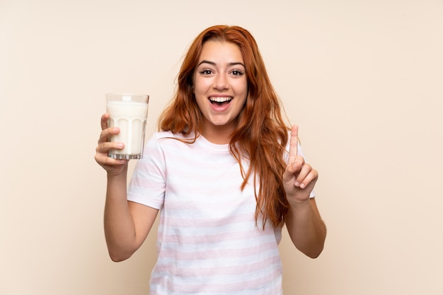 Teenager redhead girl holding a glass of milk over isolated pointing up a great idea