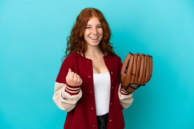 Teenager redhead girl with baseball glove isolated on blue background celebrating a victory