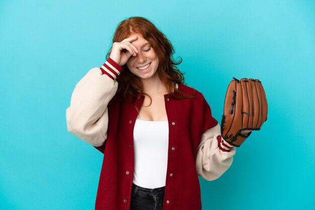 Teenager redhead girl with baseball glove isolated on blue background laughing