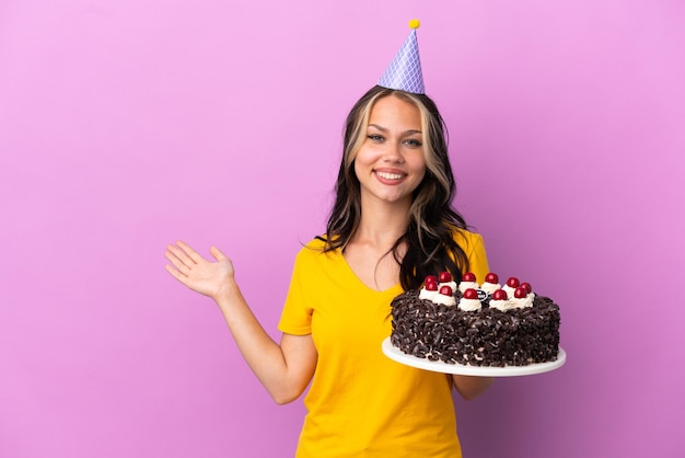 Teenager Russian girl holding birthday cake isolated on purple background extending hands to the side for inviting to come