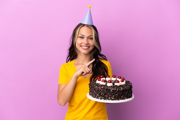 Teenager Russian girl holding birthday cake isolated on purple background pointing to the side to present a product