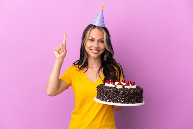 Teenager Russian girl holding birthday cake isolated on purple background pointing up a great idea