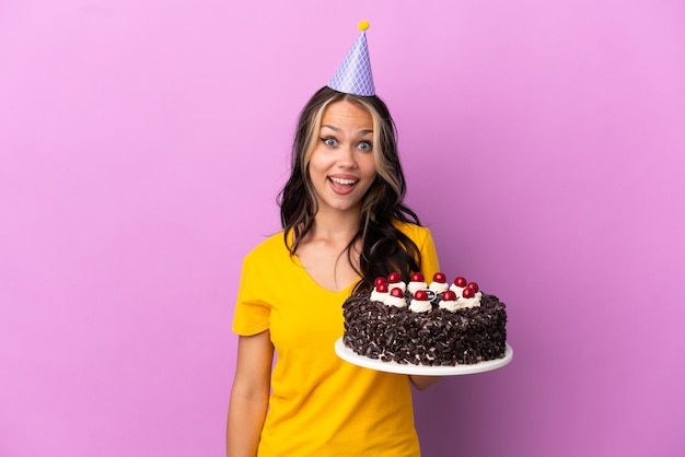 Teenager Russian girl holding birthday cake isolated on purple background with surprise facial expression