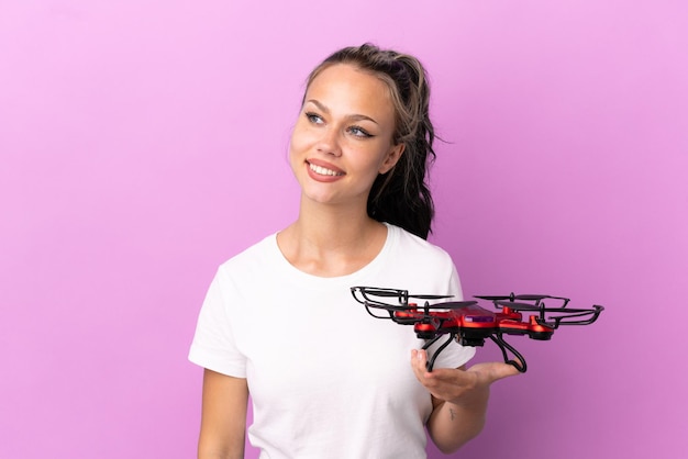 Teenager Russian girl holding a drone isolated on purple background looking to the side and smiling