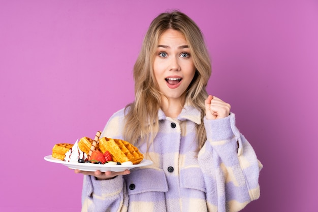 Teenager Russian girl holding waffles isolated on purple