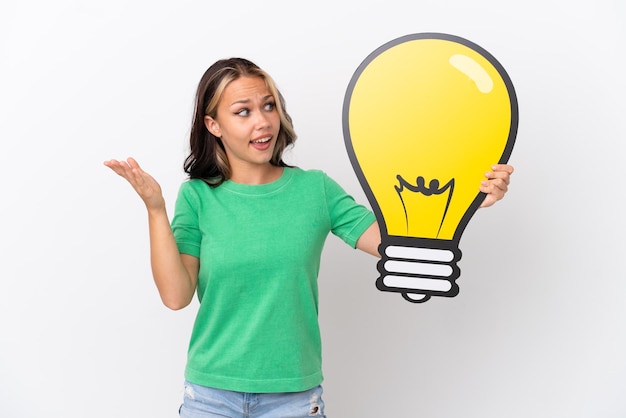 Teenager Russian girl isolated on blue background holding a bulb icon with surprised expression