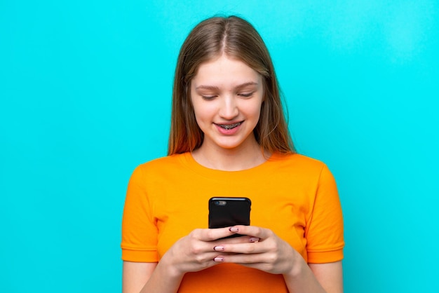 Teenager Russian girl isolated on blue background sending a message or email with the mobile