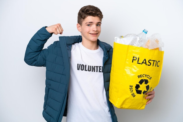 Teenager Russian holding a bag full of plastic bottles to recycle on white background doing strong gesture