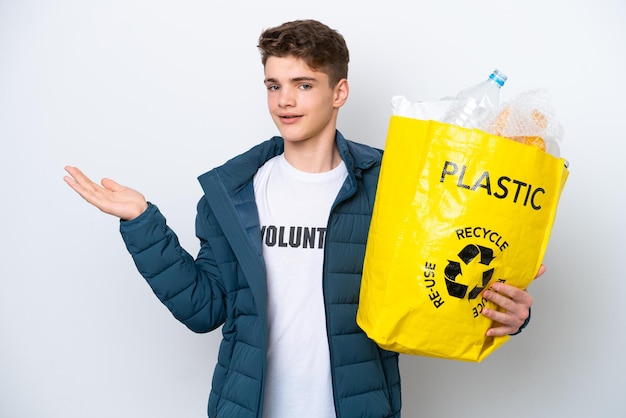 Teenager Russian holding a bag full of plastic bottles to recycle on white background extending hands to the side for inviting to come