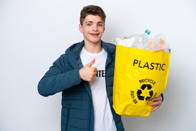 Teenager Russian holding a bag full of plastic bottles to recycle on white background giving a thumbs up gesture