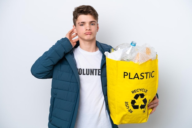 Teenager Russian holding a bag full of plastic bottles to recycle on white background having doubts