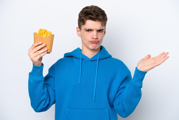 Teenager Russian man holding fried potatoes isolated on white background having doubts while raising hands