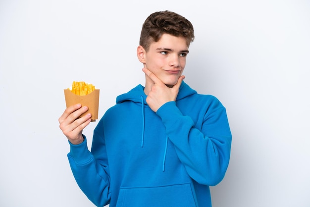 Teenager Russian man holding fried potatoes isolated on white background having doubts