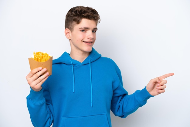 Teenager Russian man holding fried potatoes isolated on white background pointing finger to the side