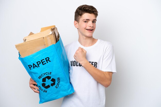 Teenager Russian man holding a recycling bag full of paper to recycle isolated on white background celebrating a victory