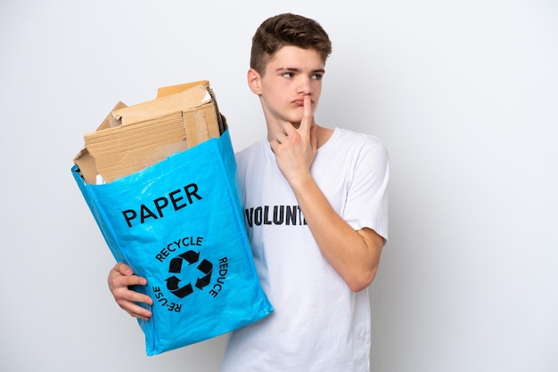 Teenager Russian man holding a recycling bag full of paper to recycle isolated on white background having doubts while looking up