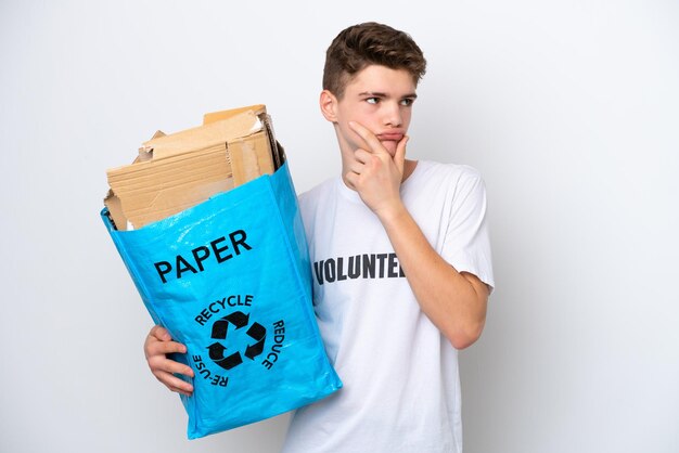 Teenager Russian man holding a recycling bag full of paper to recycle isolated on white background having doubts