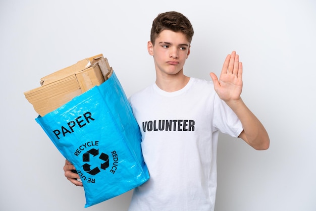 Teenager Russian man holding a recycling bag full of paper to recycle isolated on white background making stop gesture and disappointed