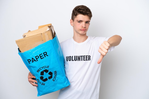 Teenager Russian man holding a recycling bag full of paper to recycle isolated on white background showing thumb down with negative expression