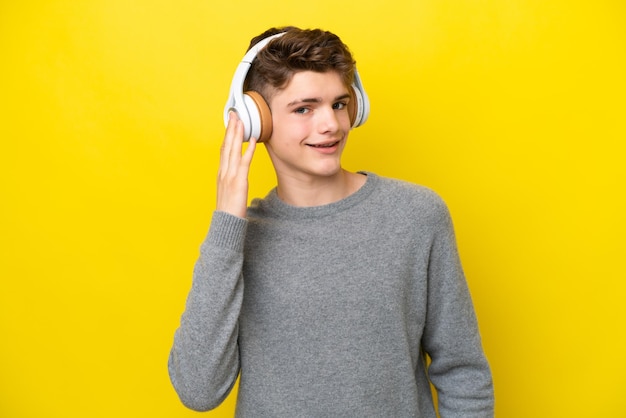 Teenager Russian man isolated on yellow background listening music