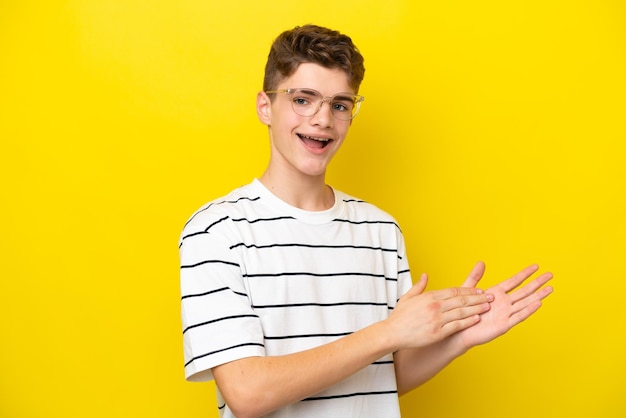 Teenager Russian man isolated on yellow background With glasses and applauding