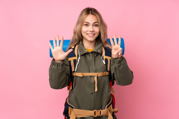 Teenager Russian mountaineer girl with a big backpack on pink wall counting eight with fingers