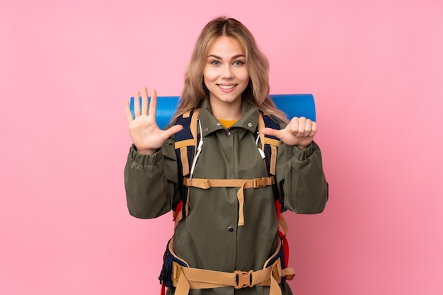 Teenager Russian mountaineer girl with a big backpack on pink wall counting six with fingers