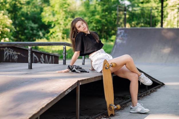 Teenager skater girl with a skateboard sitting in the skaters park