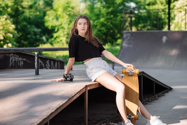 Teenager skater girl with a skateboard sitting in the skaters park