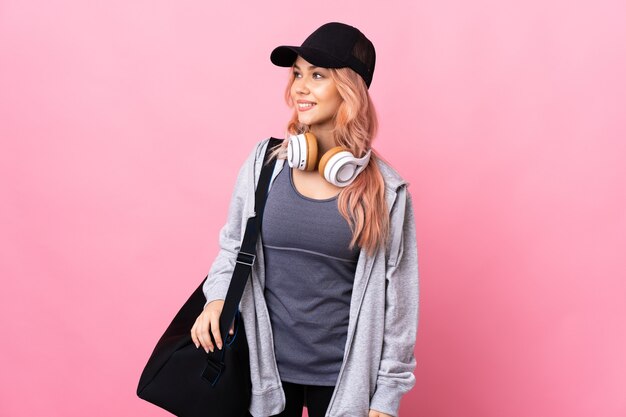 Teenager sport woman with sport bag over isolated wall looking to the side and smiling