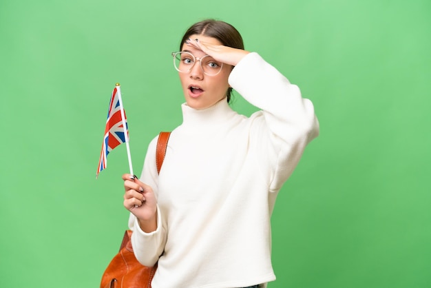 Teenager student caucasian girl holding an United Kingdom flag over isolated background doing surprise gesture while looking to the side