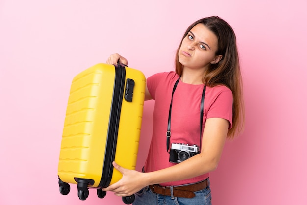 Teenager traveler girl holding a suitcase over isolated pink with sad expression