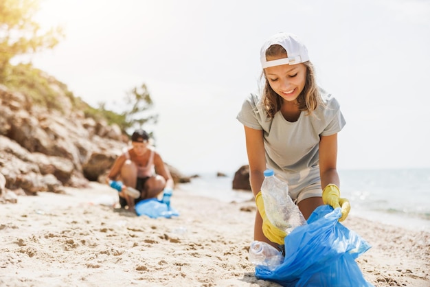 Teenager volunteers cleaning the sea beach by collecting garbage into plastic bag.