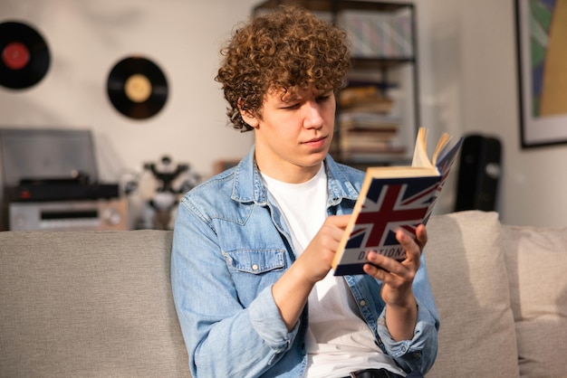 A teenager with curly hair sits focused in a room studying for an english exam a boy in a blue jean