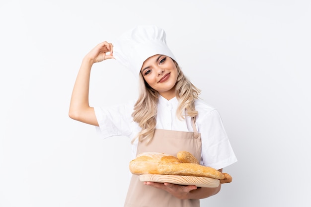 Teenager woman in chef uniform. Female baker holding a table with several breads over isolated white laughing