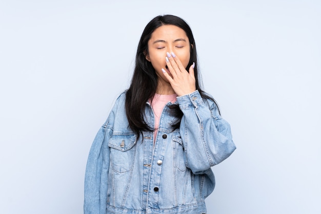 Teenager woman isolated on blue yawning and covering wide open mouth with hand