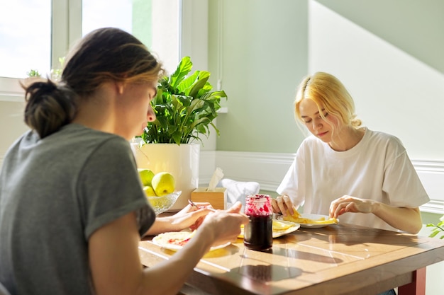 Teenagers guy and girl eating pancakes with jam sitting at table at home