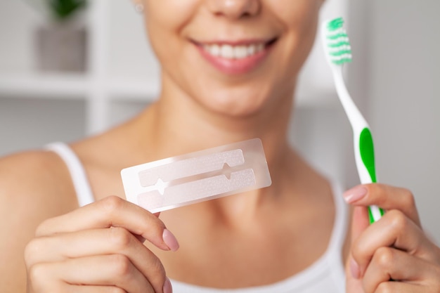 Teeth whitening, beautiful smiling woman holding a whitening strip