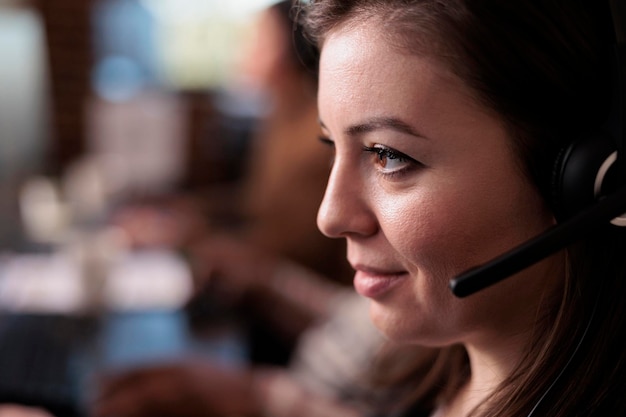 Telecommunication receptionist answering client call on headset, talking to people on remote helpline support. Young telework operator using customer care service equipment. Close up.