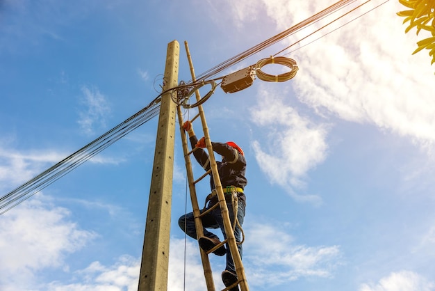 A telecoms worker is shown working from a utility pole ladder while wearing high visibility personal safety clothing PPE and a hard hatx9