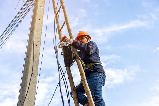 A telecoms worker is shown working from a utility pole ladder while wearing high visibility personal safety clothing PPE and a hard hatx9