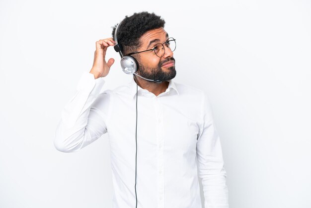 Telemarketer Brazilian man working with a headset isolated on white background having doubts and with confuse face expression